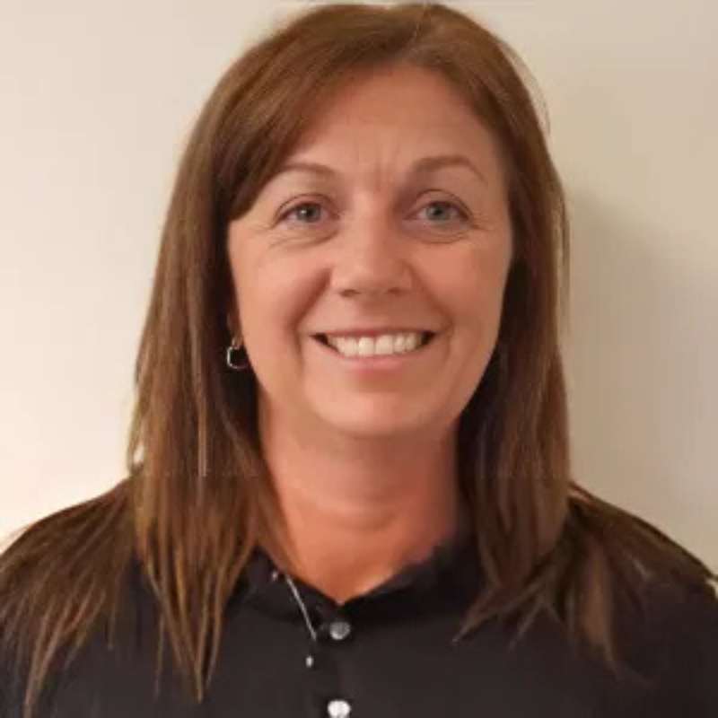 A smiling person with brown hair and a black shirt is posed against a plain, light-colored background. No landmarks or historical buildings visible.