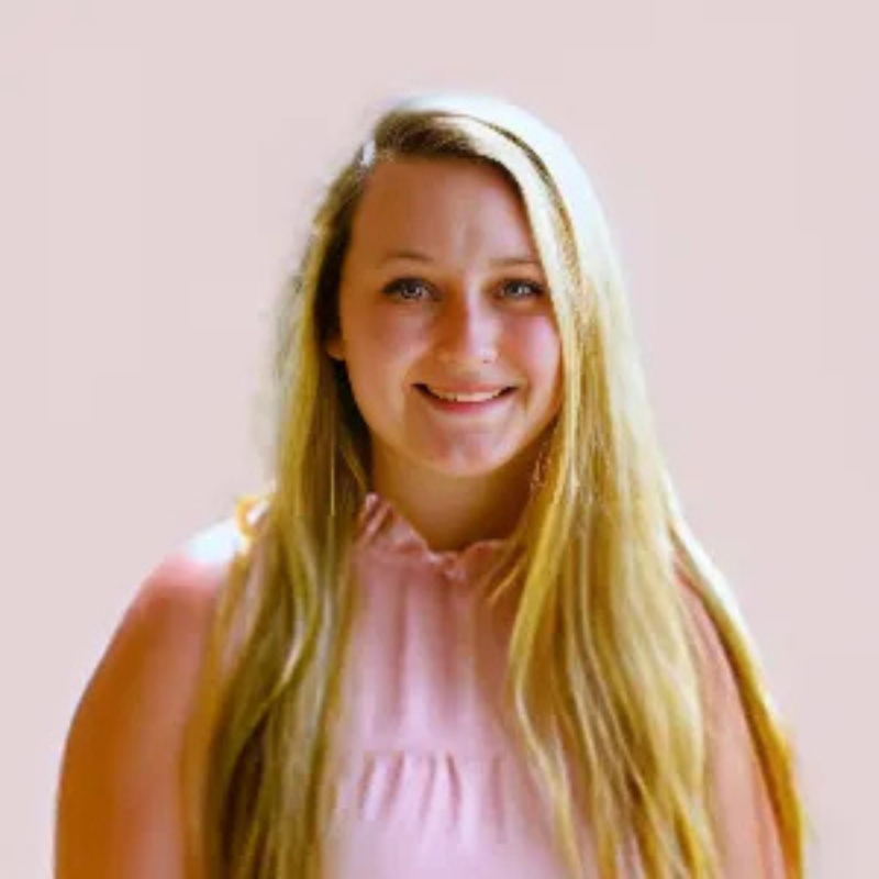 A person with long blond hair and a pink blouse smiles against a plain background. No landmarks or historical buildings are visible.