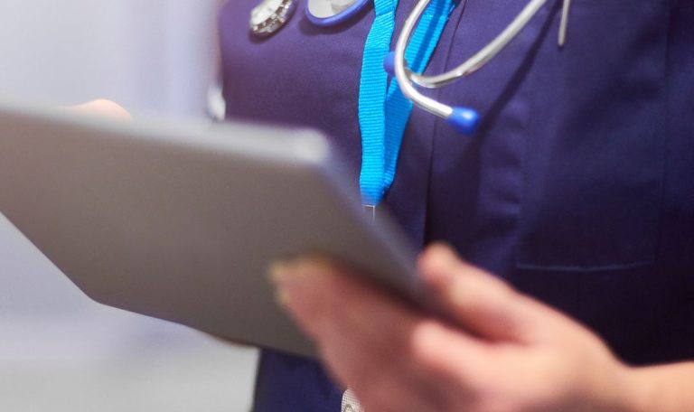 A person in a medical uniform with a stethoscope uses a tablet, suggesting a healthcare setting or activity.