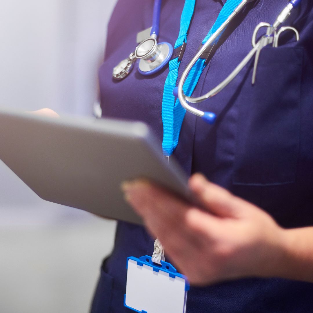 A person in a medical uniform with a stethoscope uses a tablet, suggesting a healthcare setting or activity.