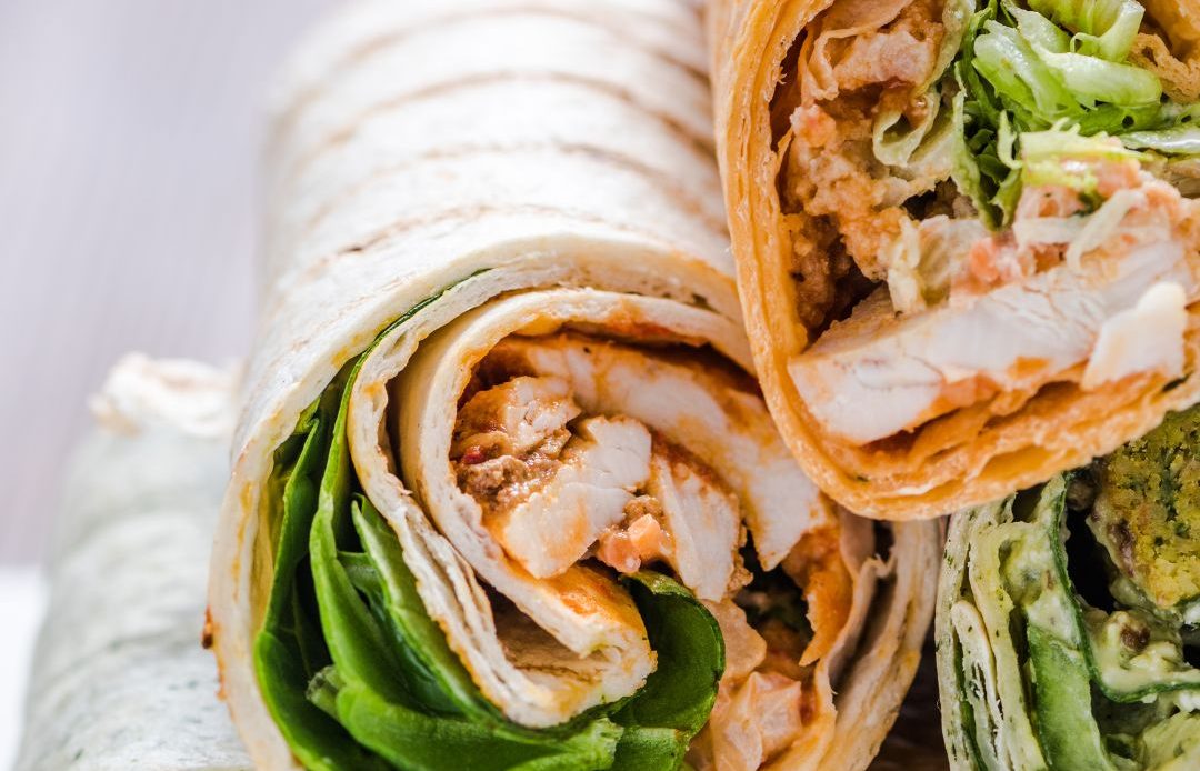 A close-up of three wraps, filled with grilled chicken, fresh lettuce, and various sauces, showcasing a delicious, vibrant selection of flavors.
