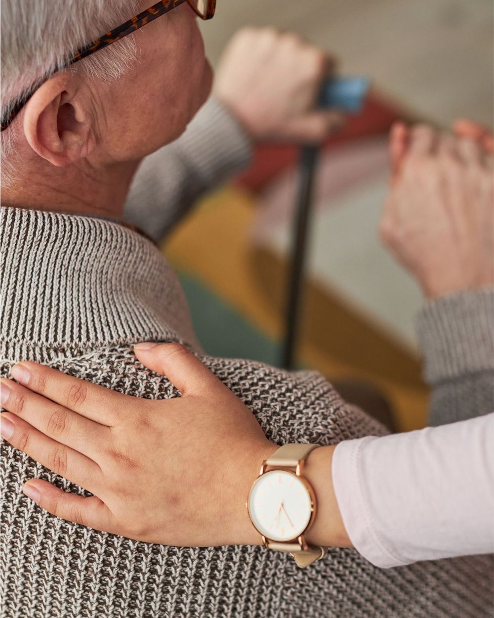 A person with glasses uses a mobility aid, another person&#039;s hand gently on their shoulder, offering support and comfort in a caring manner.