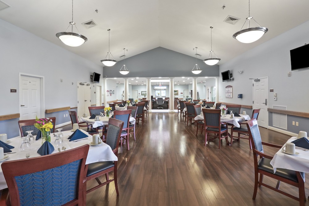 Assisted Living 25 Spacious dining area with neatly arranged tables and chairs, elegant lighting, and floral centerpieces, set in a well-lit, modern interior space.