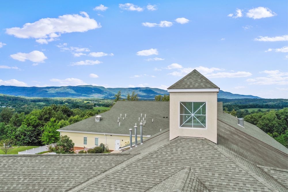 Assisted Living 38 Rooftop with a cupola overlooks a lush, green landscape with distant mountains under a bright, blue sky. There's a yellow building visible.