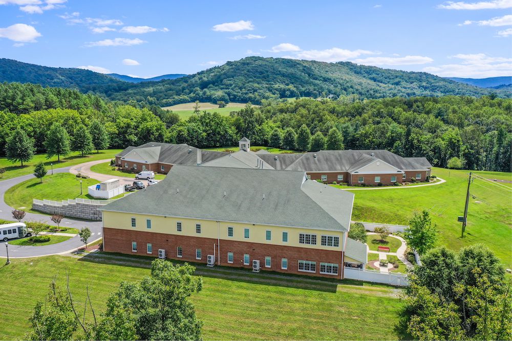 Assisted Living 37 A large, modern building complex with a brick exterior is surrounded by grassy fields and hills under a partly cloudy sky.