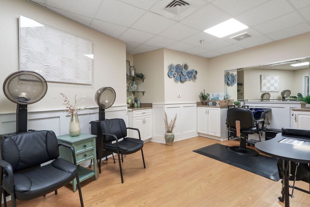 Assisted Living 7 Cozy hair salon interior with styling chairs, drying stations, decorative vases, and wall art. Natural light illuminates the tidy, welcoming space.