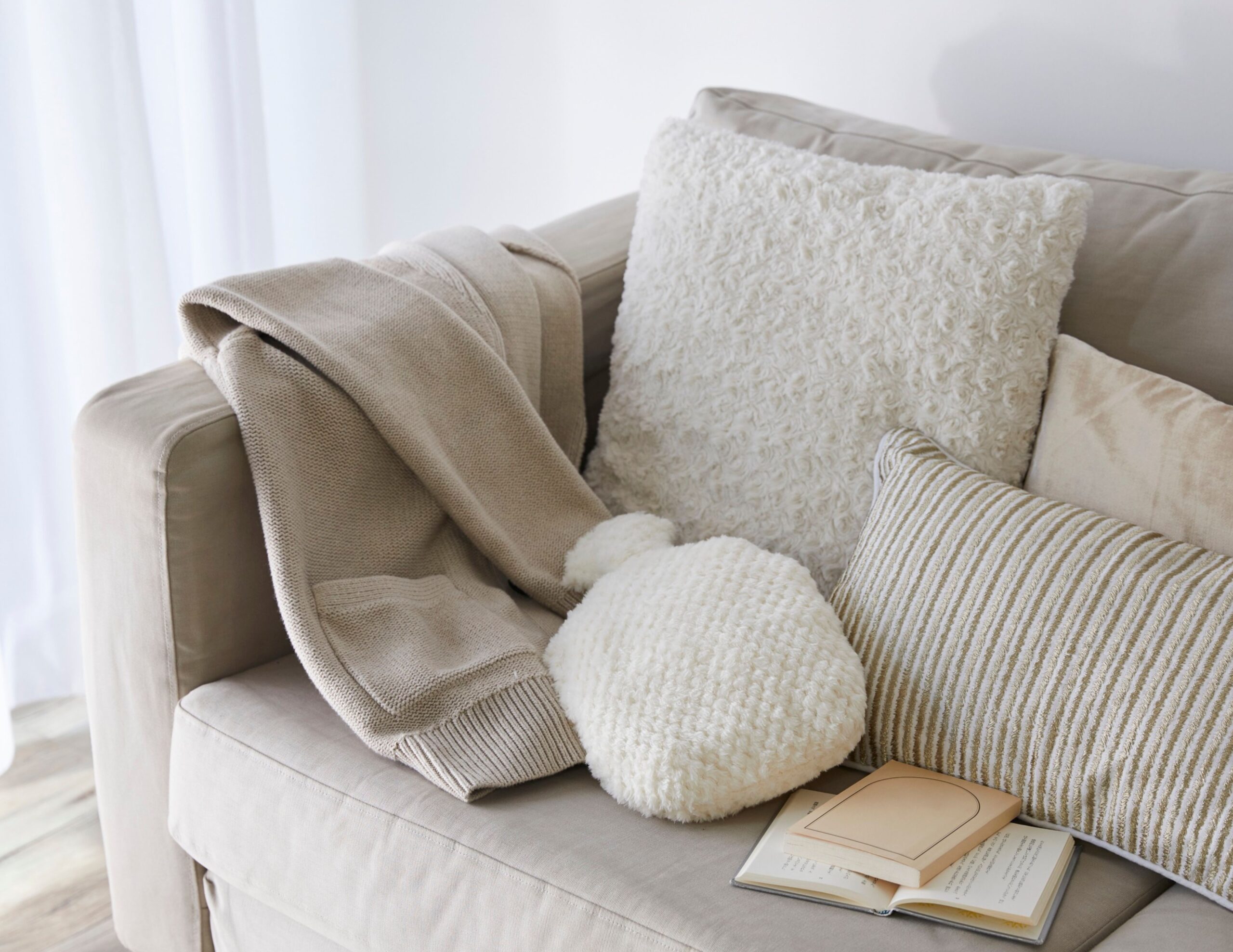 Home 4 A cozy sofa with textured pillows, soft blanket, and an open book. Bright and inviting atmosphere in a serene living space.
