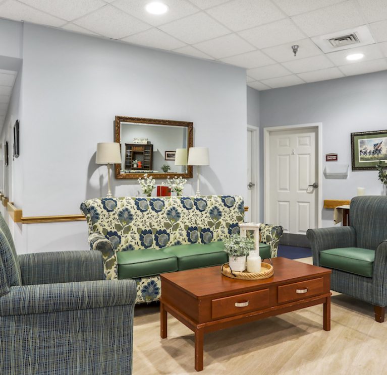 A cozy sitting area features patterned couches, armchairs, a wooden table, and framed art, creating an inviting and comfortable space.