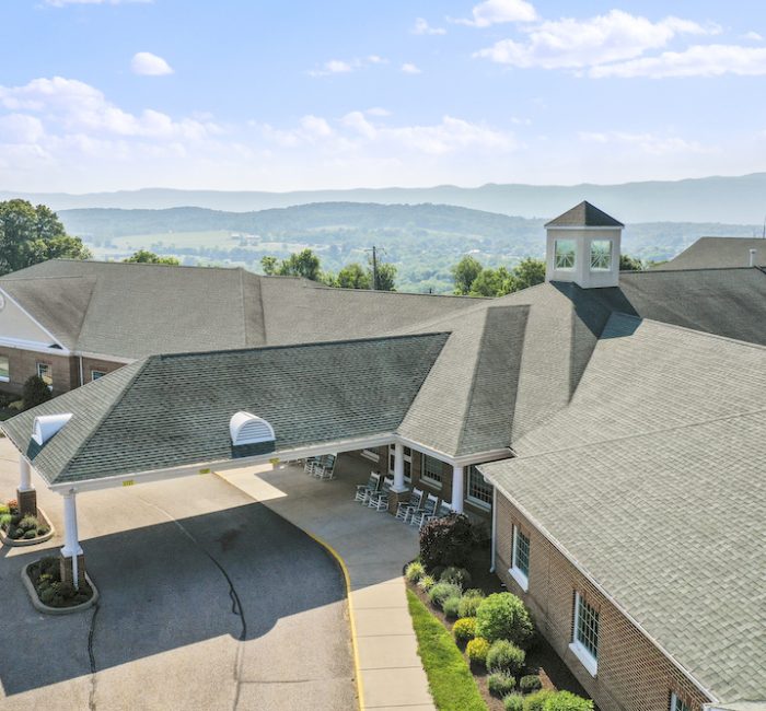 Aerial view of a sprawling building with a covered entrance. Surrounding lush landscape and distant mountains create a serene backdrop.