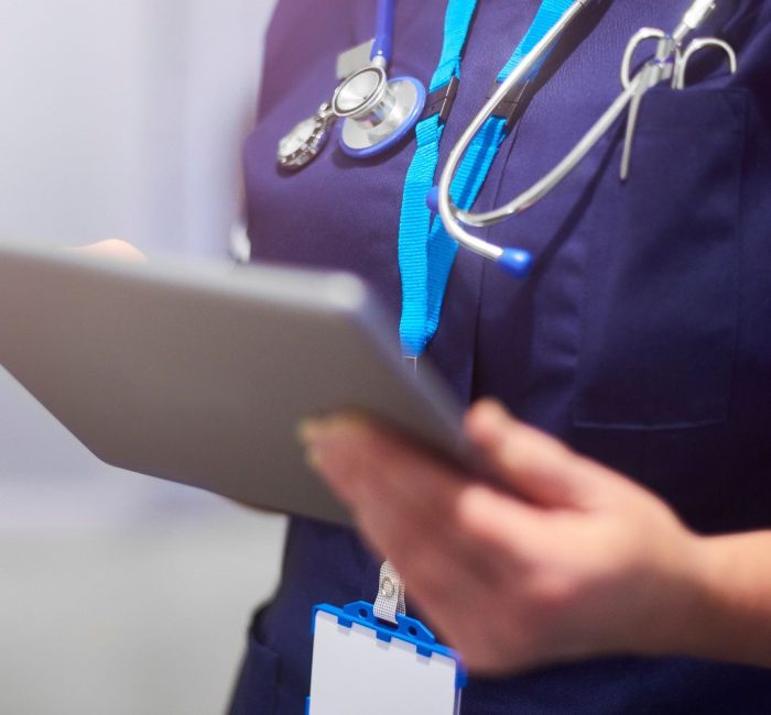 A person in a medical uniform with a stethoscope uses a tablet, suggesting a healthcare setting or activity.