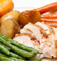 Close-up of a roasted meal featuring sliced chicken, roasted potatoes, carrots, and green beans, emphasizing texture and colors.